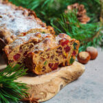 Traditional Christmas fruit cake on a wooden board in a festive decoration, dark background.