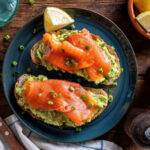 Delicious avocado and smoked salmon toasts on a rustic wood table top.
