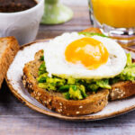 Avocado egg sandwich with whole grain bread on wooden background. Copy space